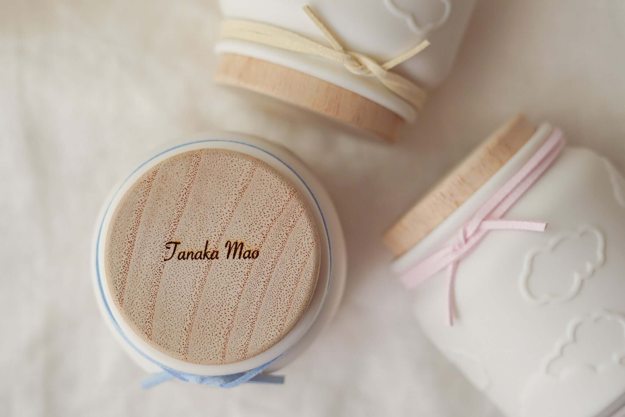 赤ちゃんのお骨壷に名前が彫刻された木製のふたとパステルカラー紐を結んだデザインの画像