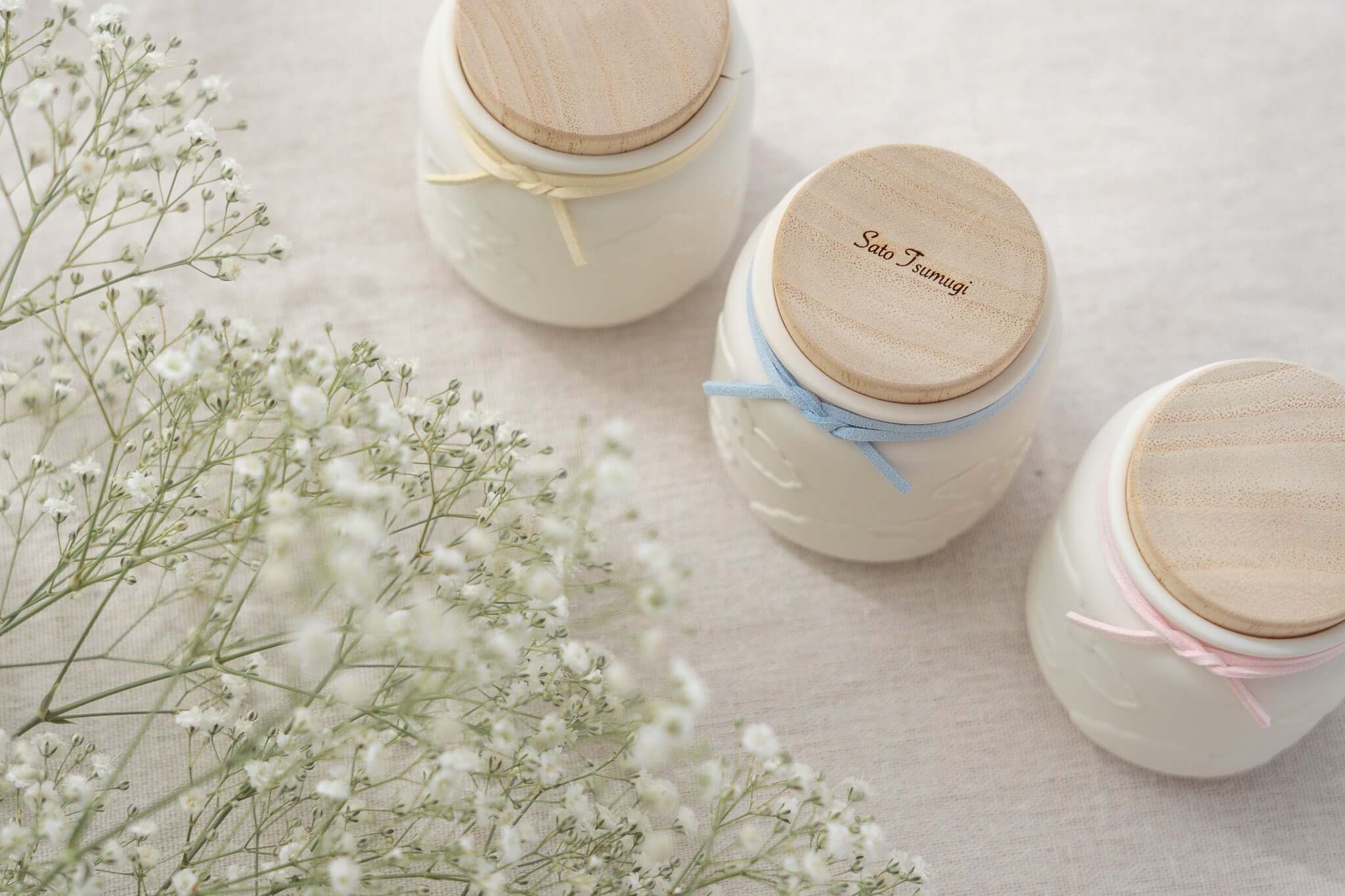 赤ちゃんのお骨壷-天使のうつわの3つの可愛らしい骨壷と小花のアレンジメントの画像