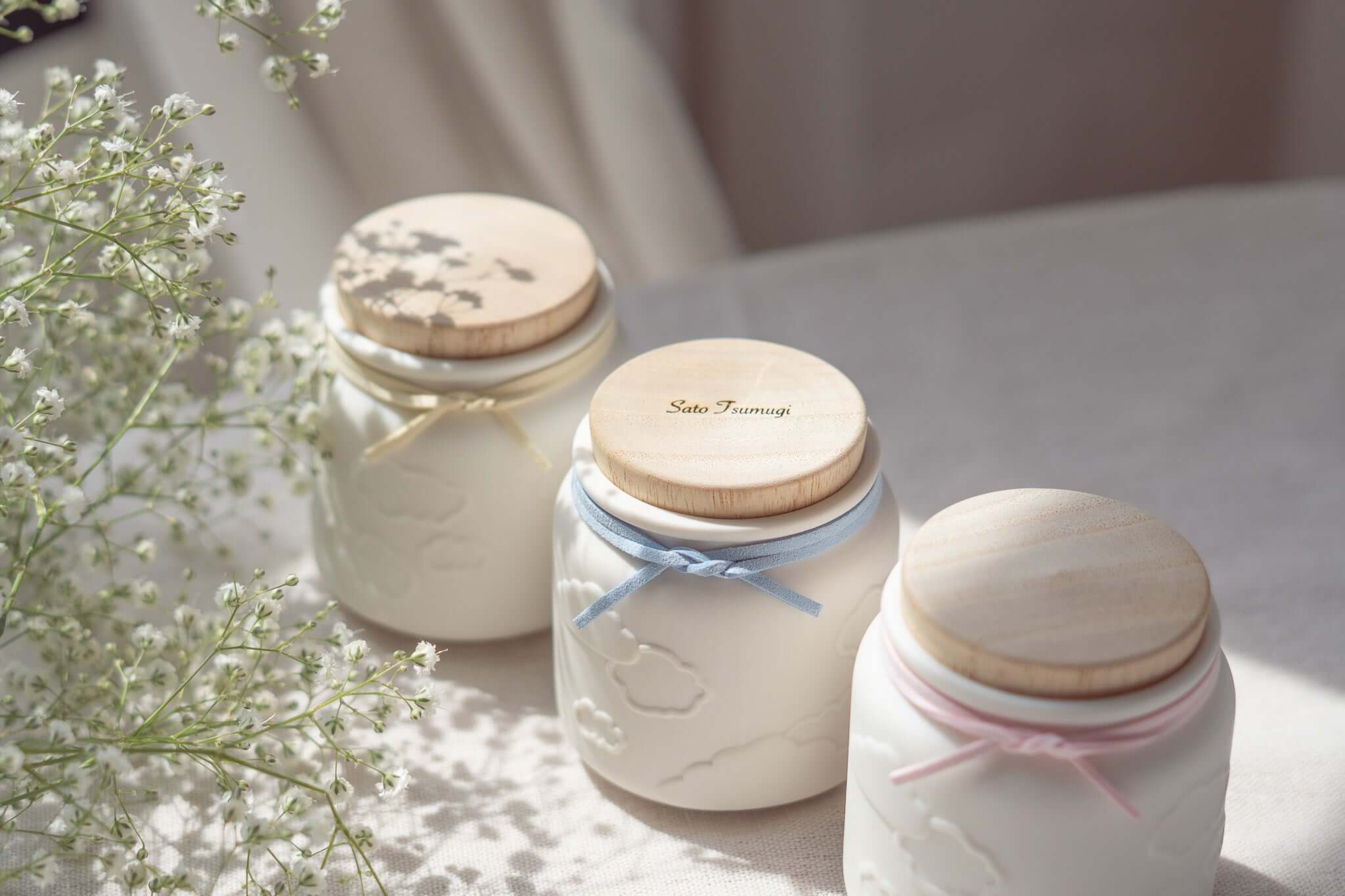 赤ちゃんのお骨壷-天使のうつわの3つの可愛らしい骨壷と小花のアレンジメントの画像